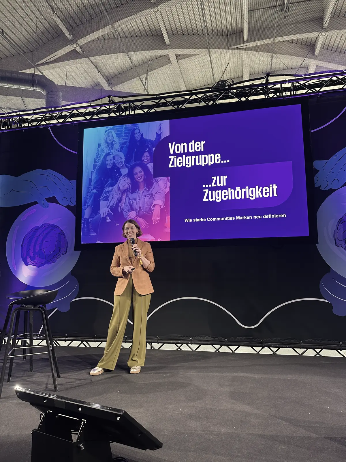 Dorothee Ebert hält eine Keynote auf einer großen Bühne vor Publikum, im Hintergrund die Präsentationsfolie zum Thema Zugehörigkeit