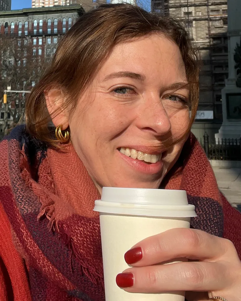 Dorothee Ebert lacht in die Kamera, eingehüllt in einen roten Schal, einen Kaffeebecher in der Hand